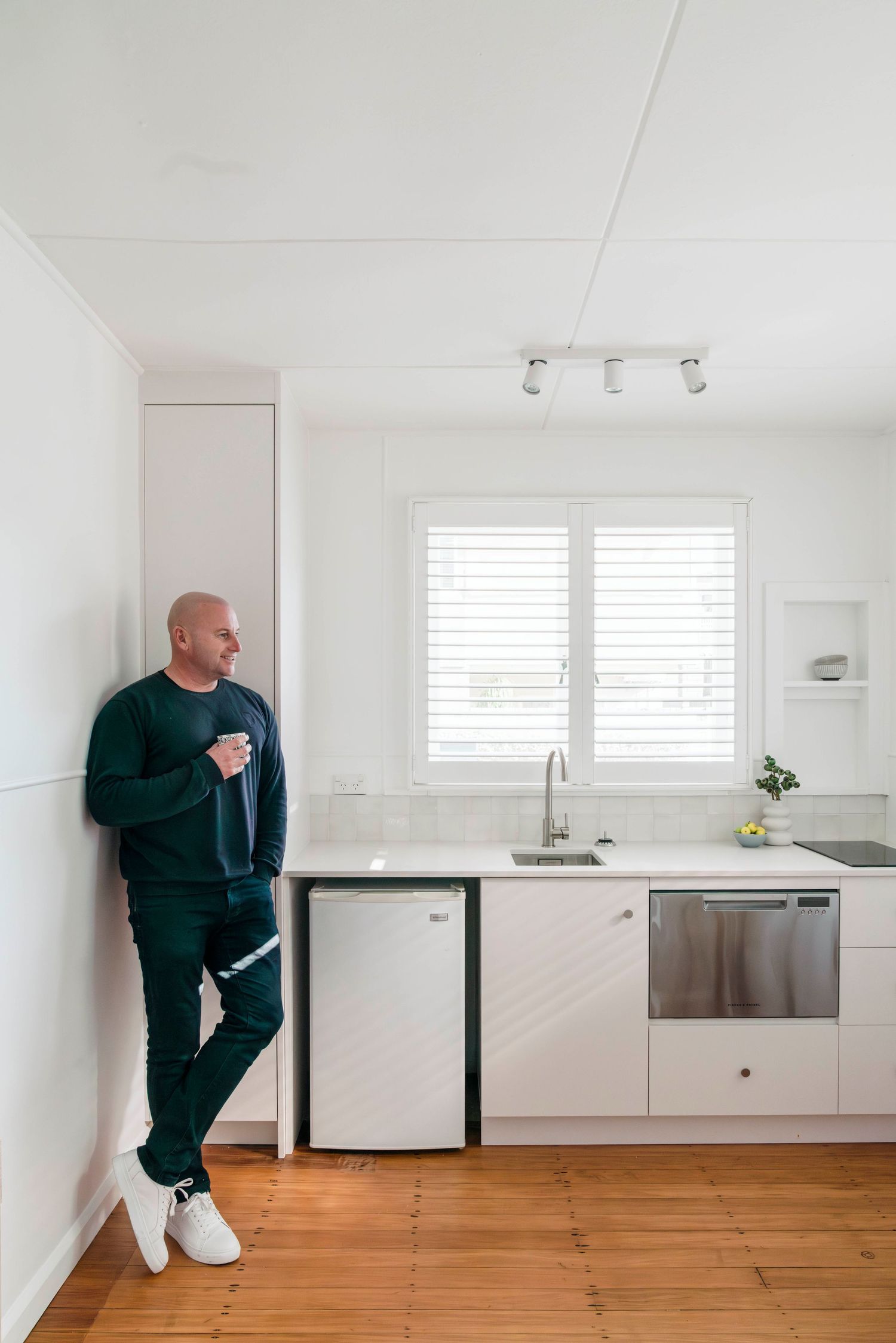 Modern minimalist kitchen interior with white cabinets, wooden flooring, and sleek appliances.