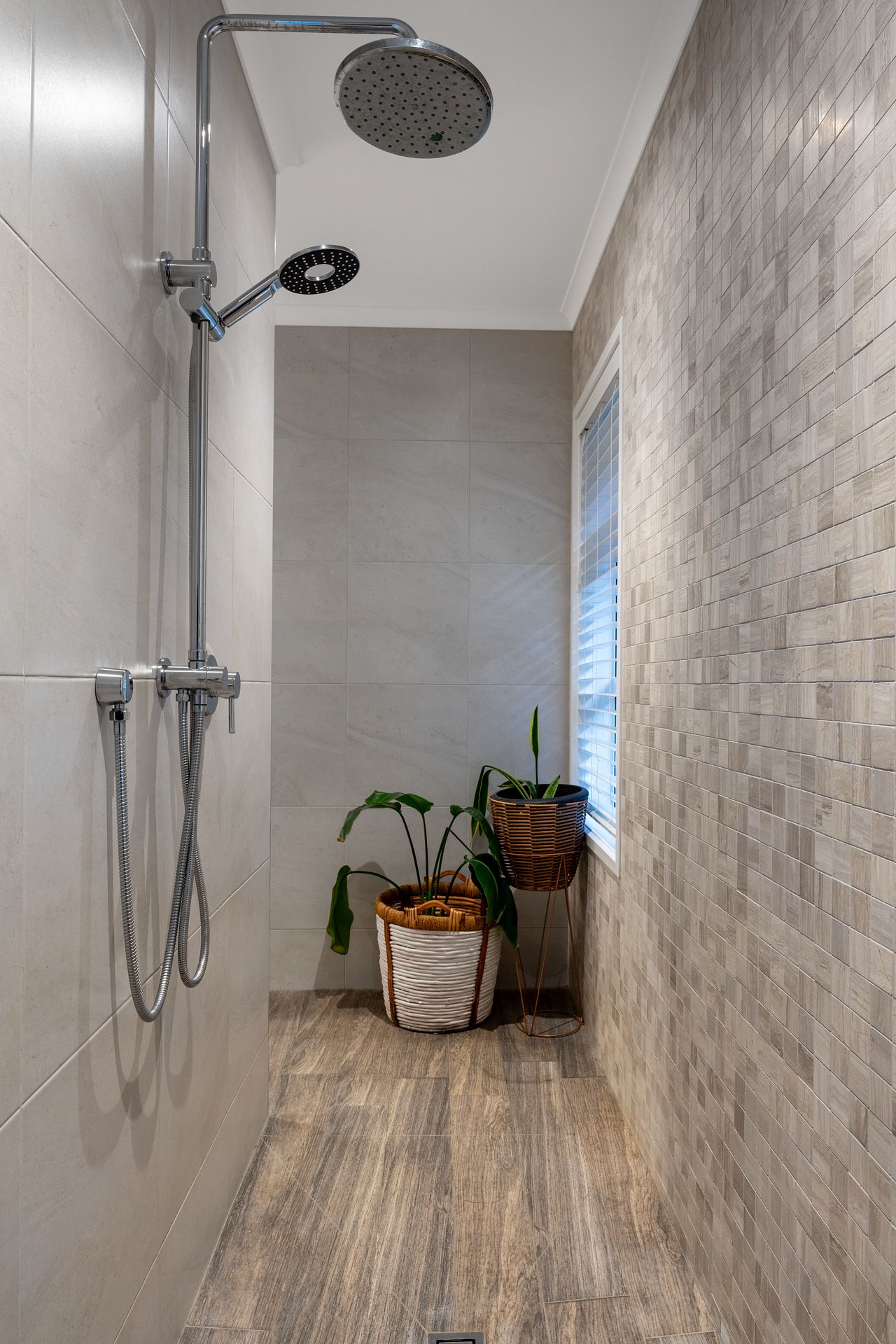 Modern walk-in shower with white textured tile walls, wood-look flooring, and rainfall showerhead mounted on exposed plumbing.