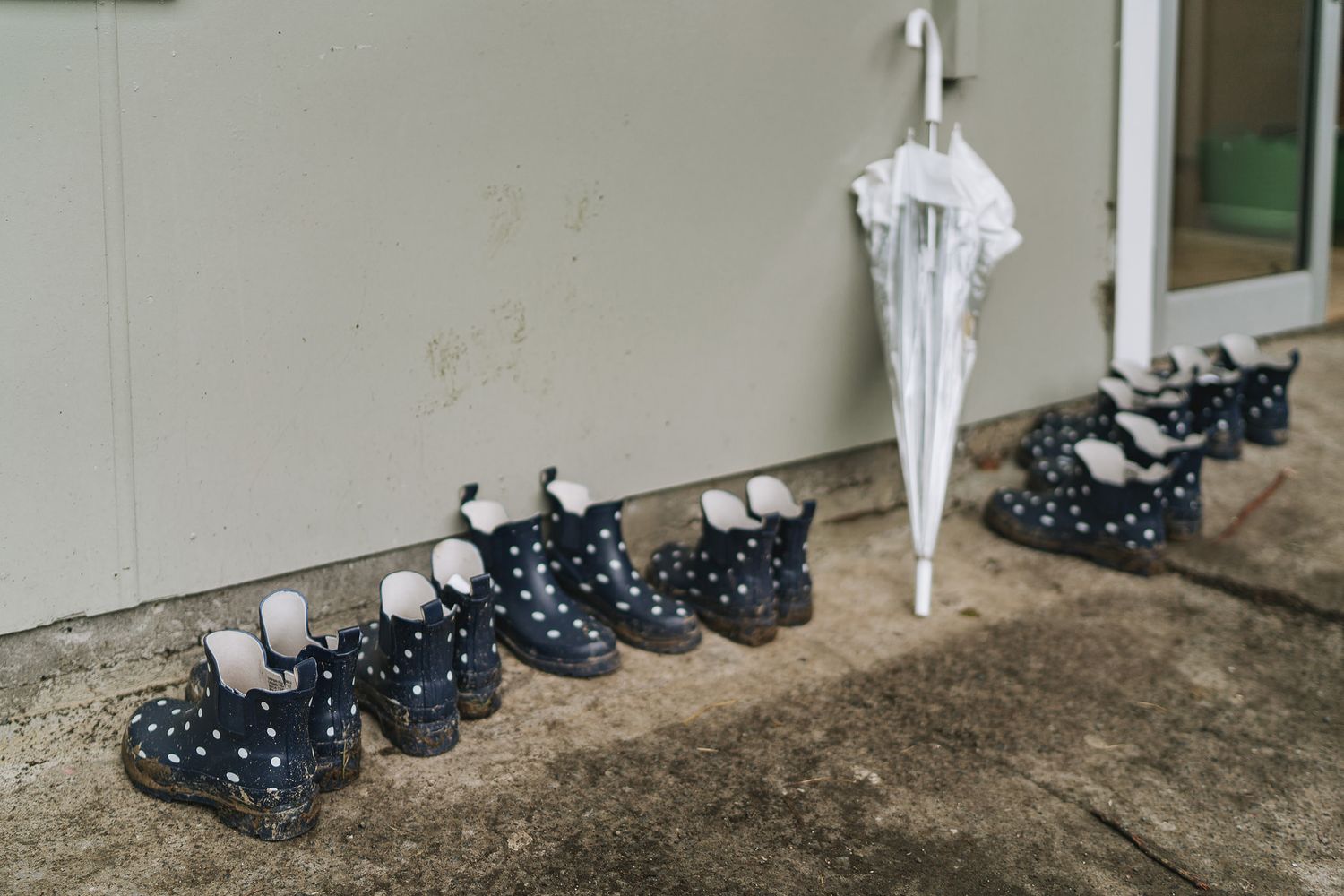 A row of polka dot rain boots lined up against a white wall on a beige floor.