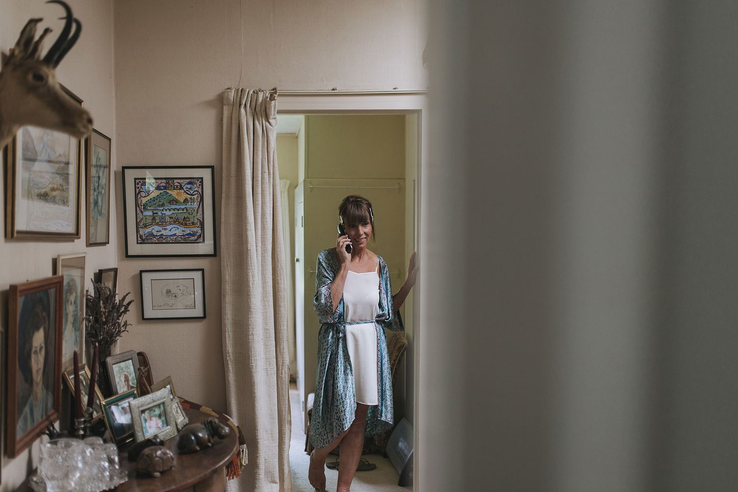 A person stands in a doorway wearing a light blue dress, photographed from a room with framed artwork on the walls.