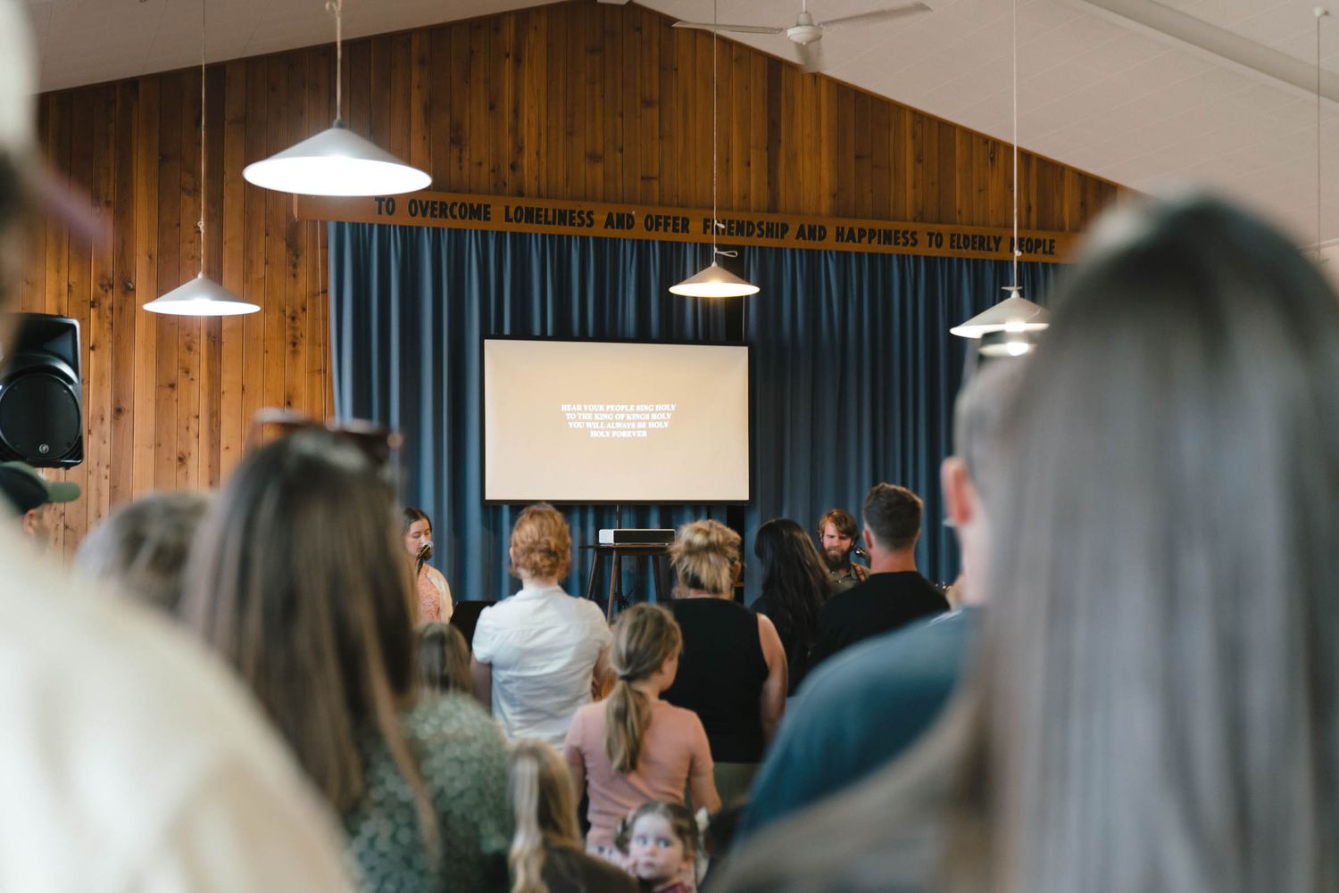 People gathered in a wood-paneled room with blue curtains and projection screen.