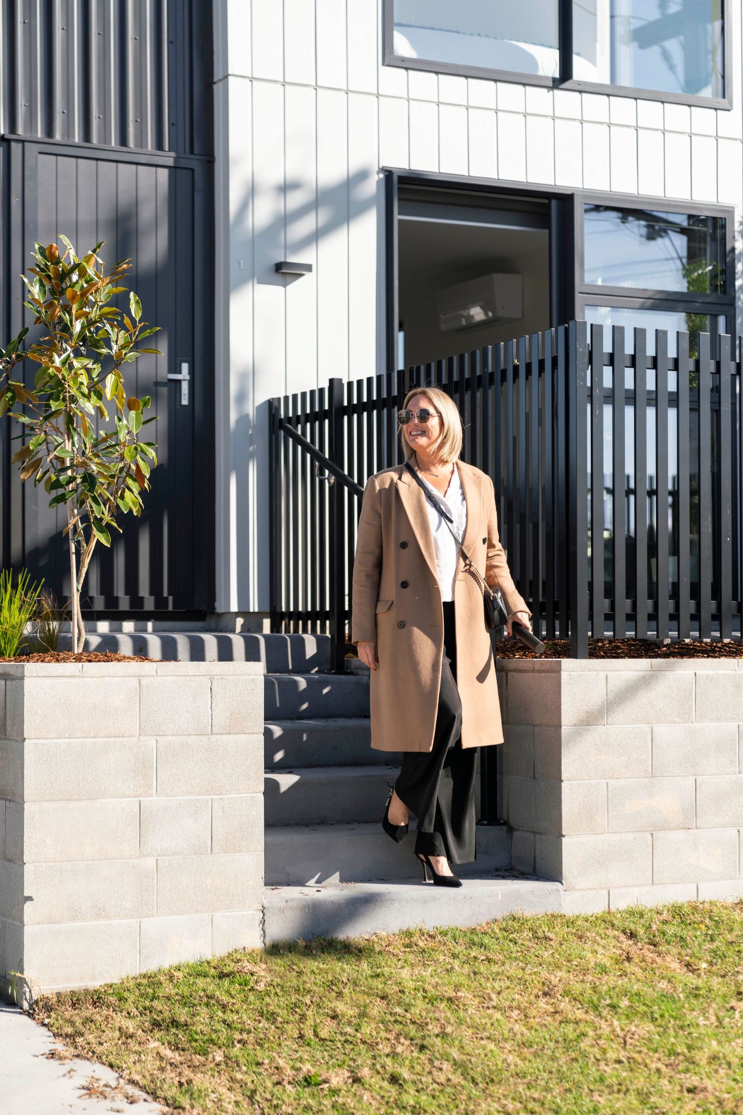 Modern home exterior featuring black metal fencing and beige stonework with lush landscaping details.