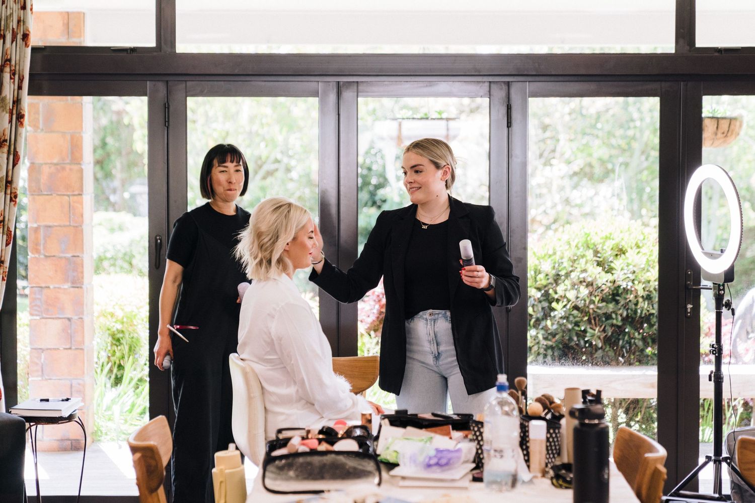 Three people in black attire working at a styling station with natural light from large windows.