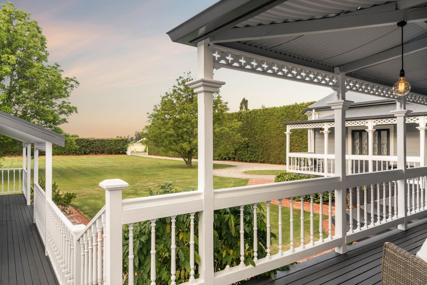 White wraparound porch with decorative railings overlooking grassy landscape at sunset.