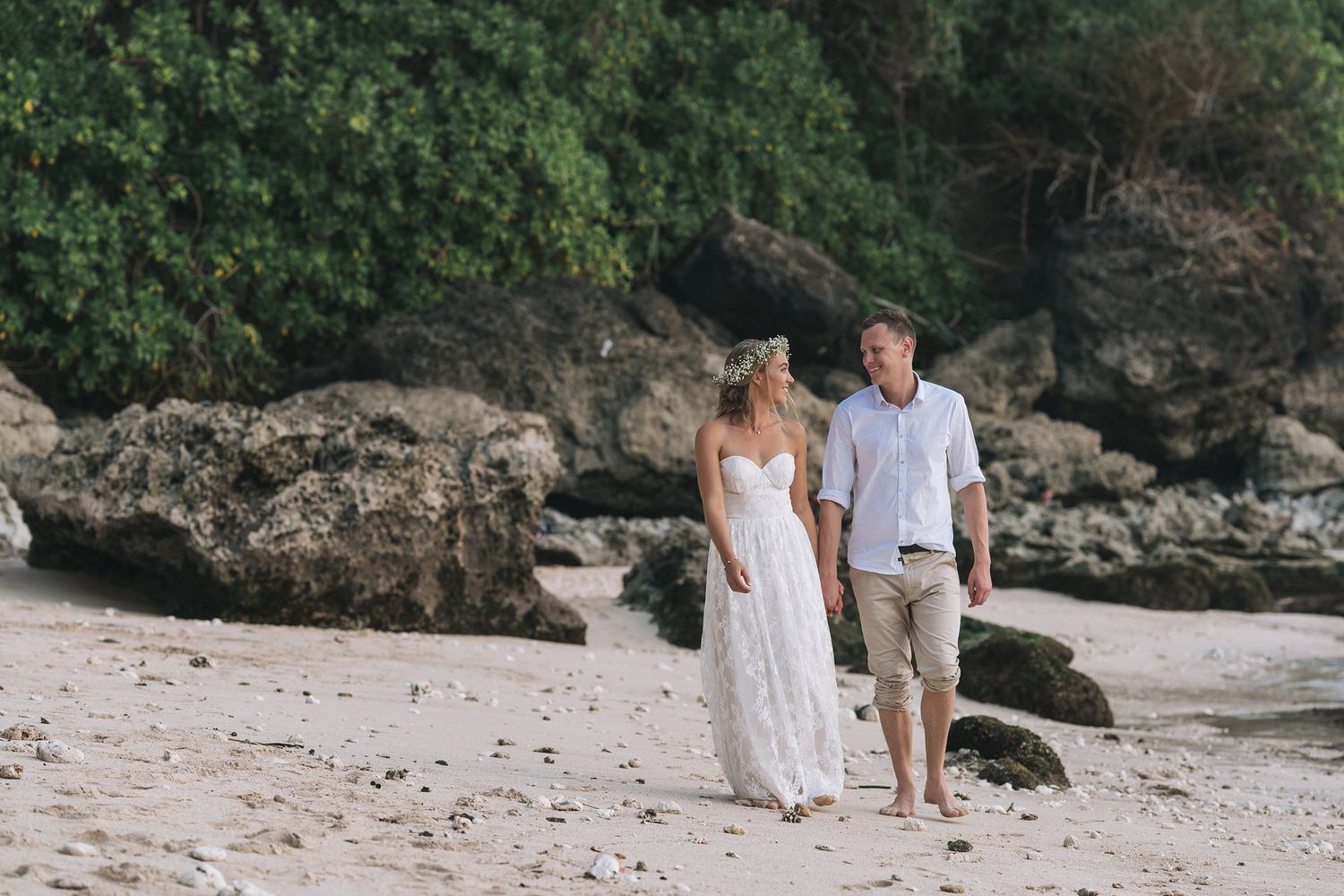 Couple walking along scenic beach with rocky cliffs in the background.