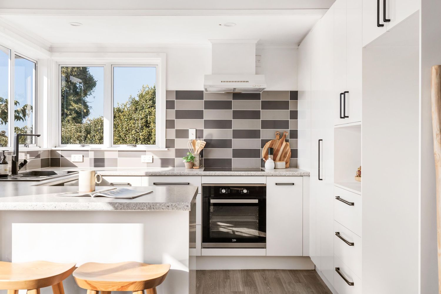 Modern white kitchen with checkered backsplash featuring sleek appliances and wooden accents.