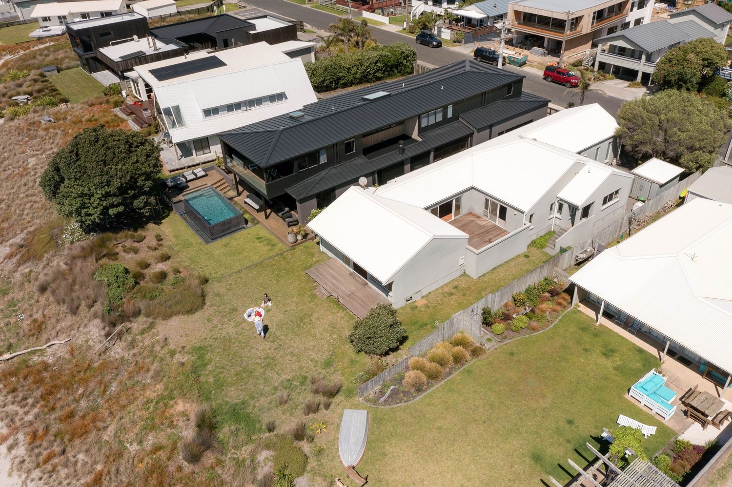 Aerial view of modern black-roofed building among white houses with swimming pools and landscaped yards.