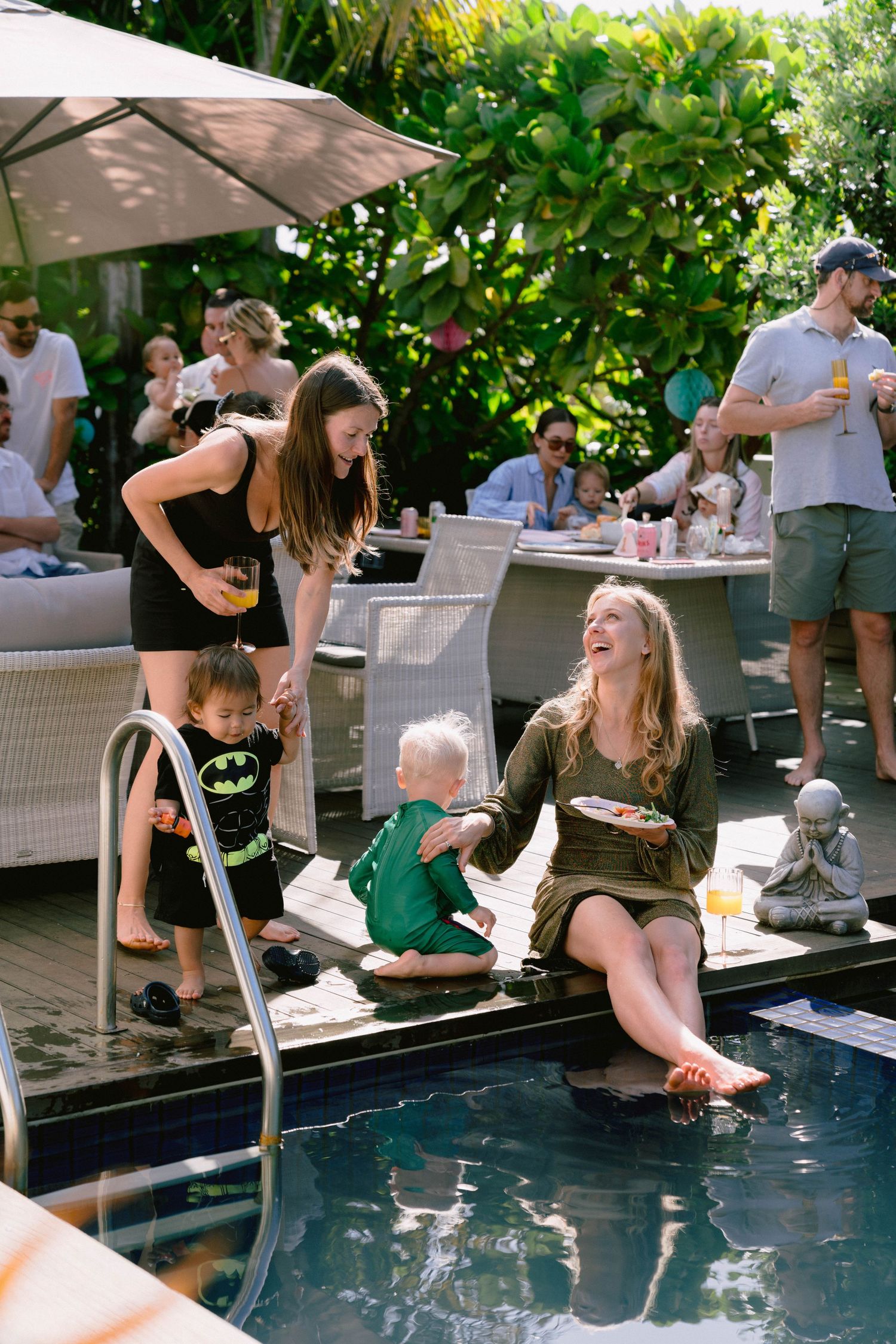 People enjoying a poolside gathering with feet dangling in the water on a sunny day.