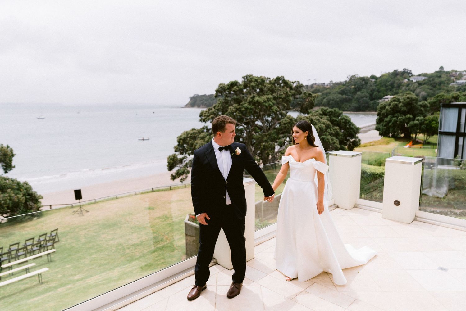 A couple holding hands during their beachside wedding ceremony with ocean views and lush greenery.