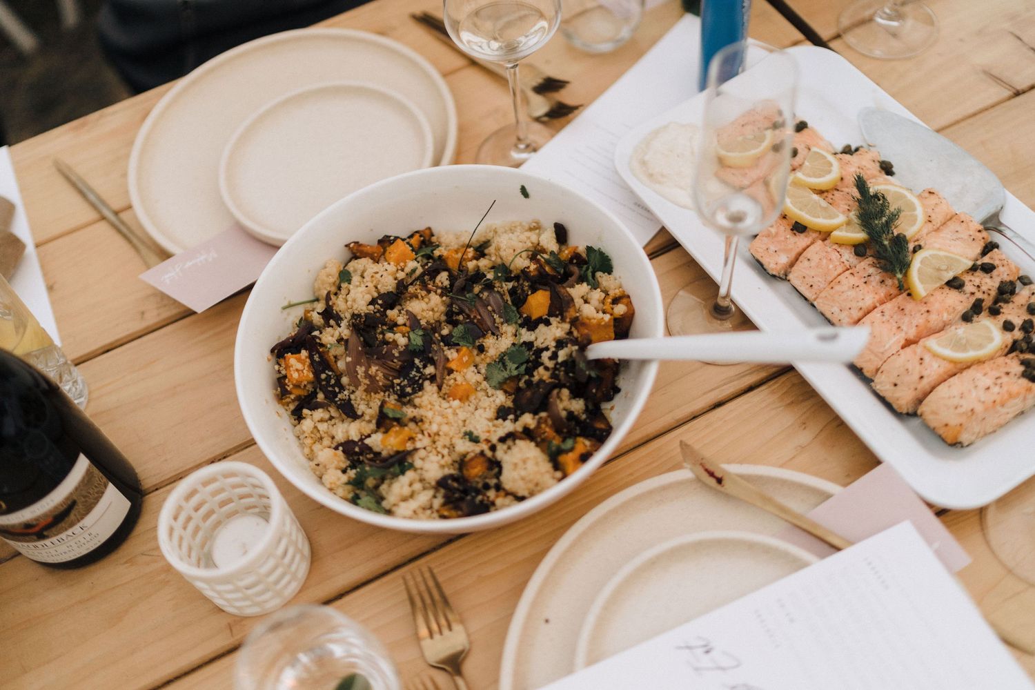 Elegant wedding reception food displayed on white plates at wooden table setting.