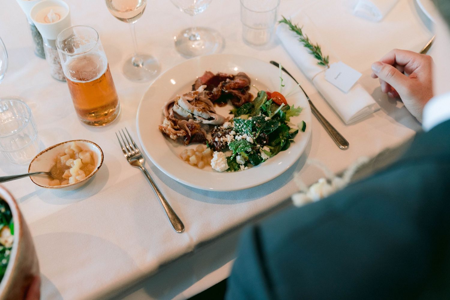 Elegant plated meal with salad and meat served on white tablecloth at formal dinner.