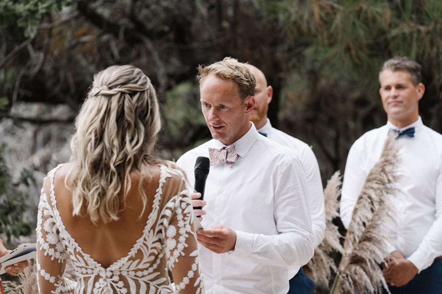 A couple exchanges vows during an outdoor wedding ceremony with lush greenery in the background.