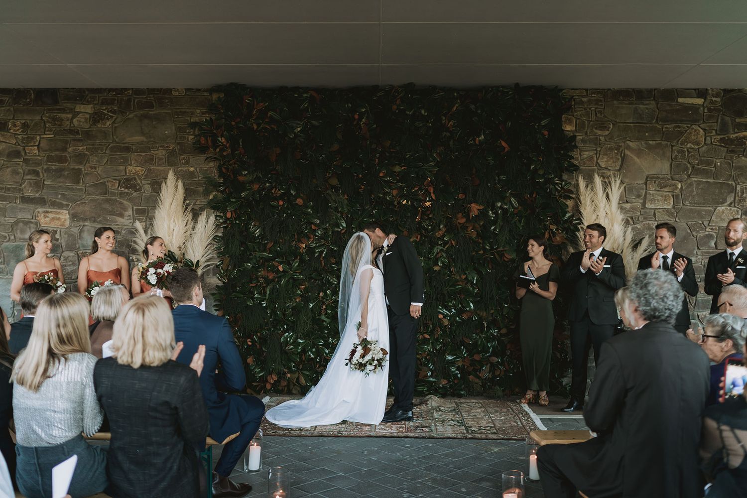 Guests celebrate at an elegant rustic wedding reception with stone walls and greenery decorations in the background.