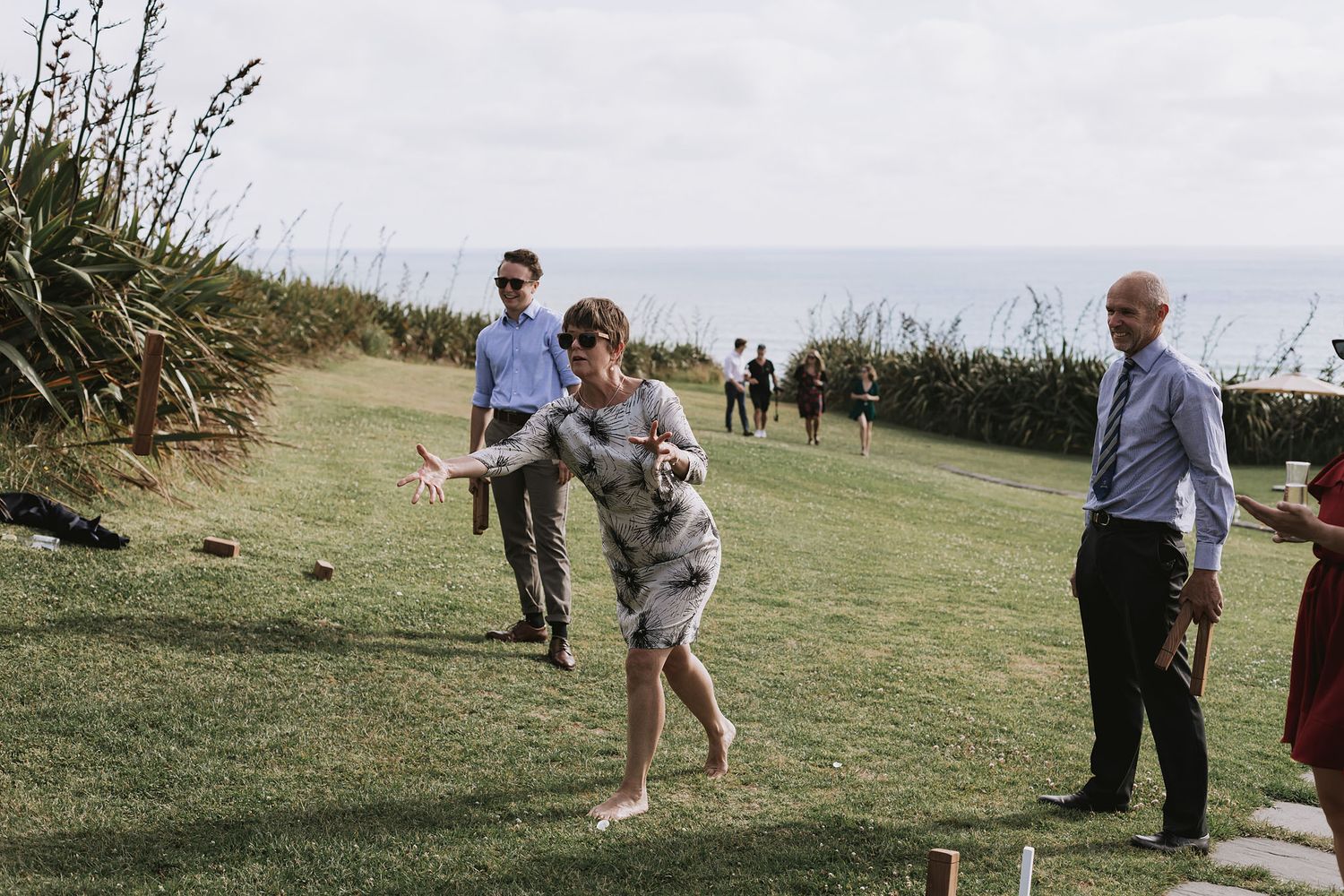 People playing lawn games outdoors on a grassy area with plants and shrubs visible in the background.