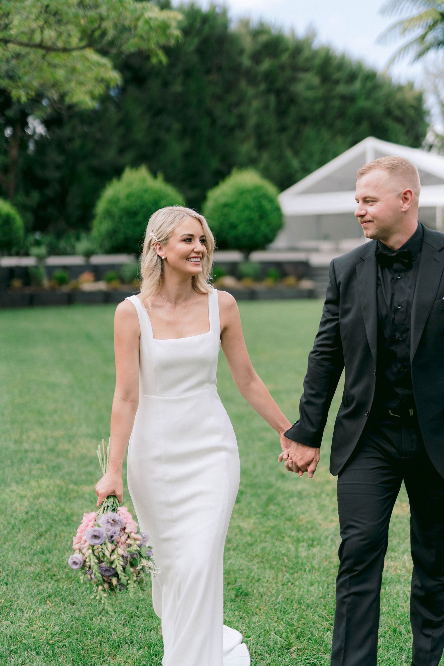 A couple walks hand in hand through a garden setting at their wedding.