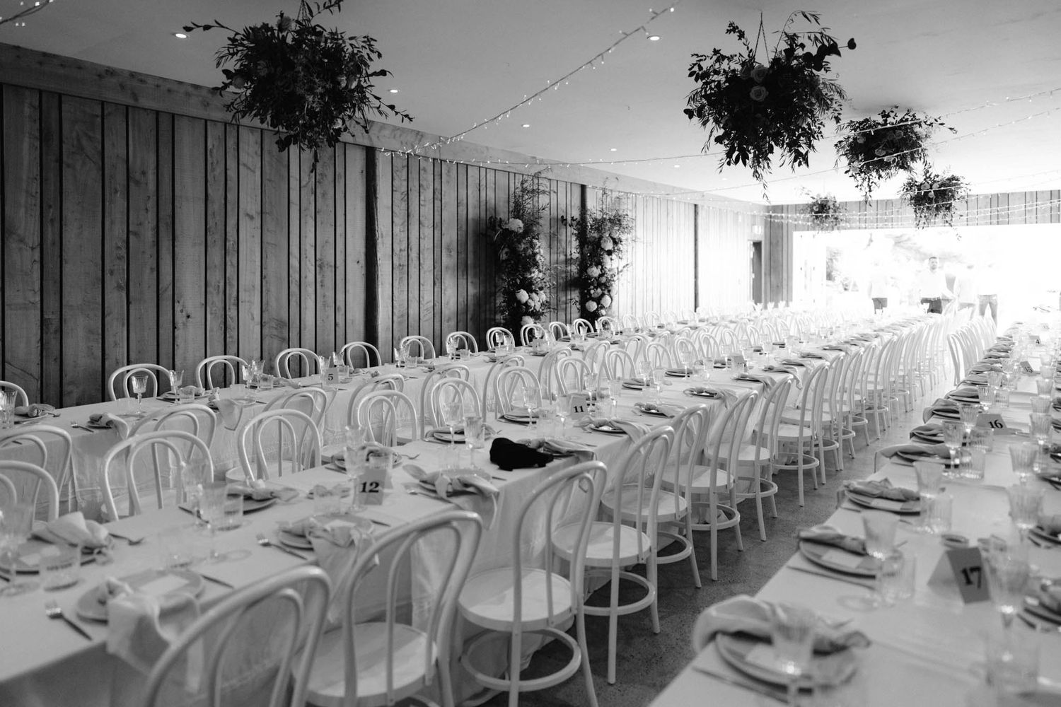 Black and white photo of an elegant wedding reception setup with long tables and hanging floral arrangements.