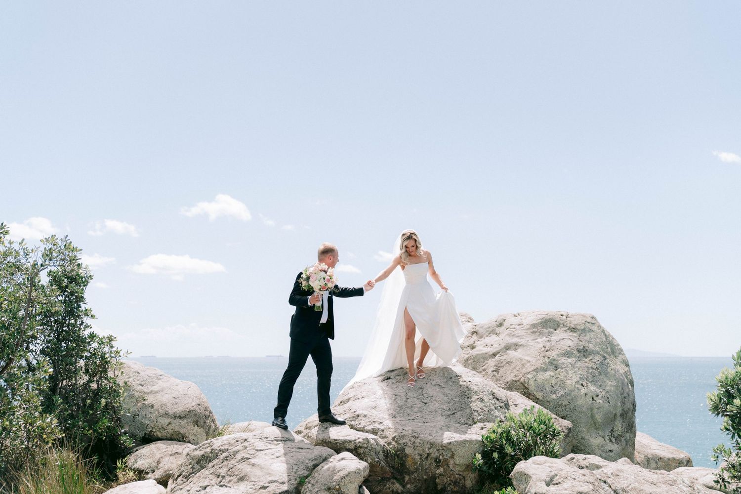 Newlywed couple poses on scenic mountain rocks during outdoor wedding photo session.