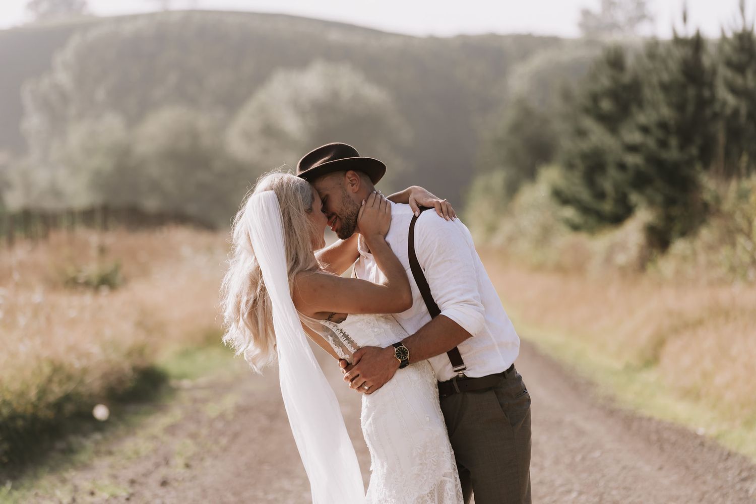 A romantic moment shared between a couple in wedding attire on a dirt path with misty mountains in the background.