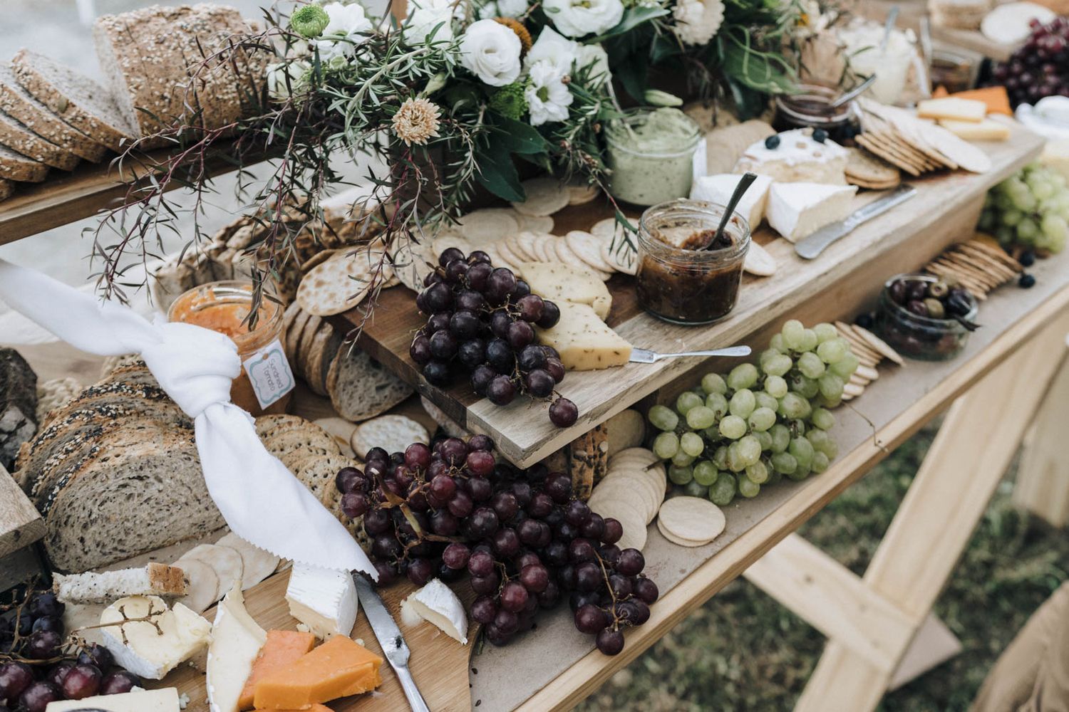 Rustic grazing board with assorted cheeses, grapes, bread, and greenery arranged on a wooden surface for elegant entertaining.