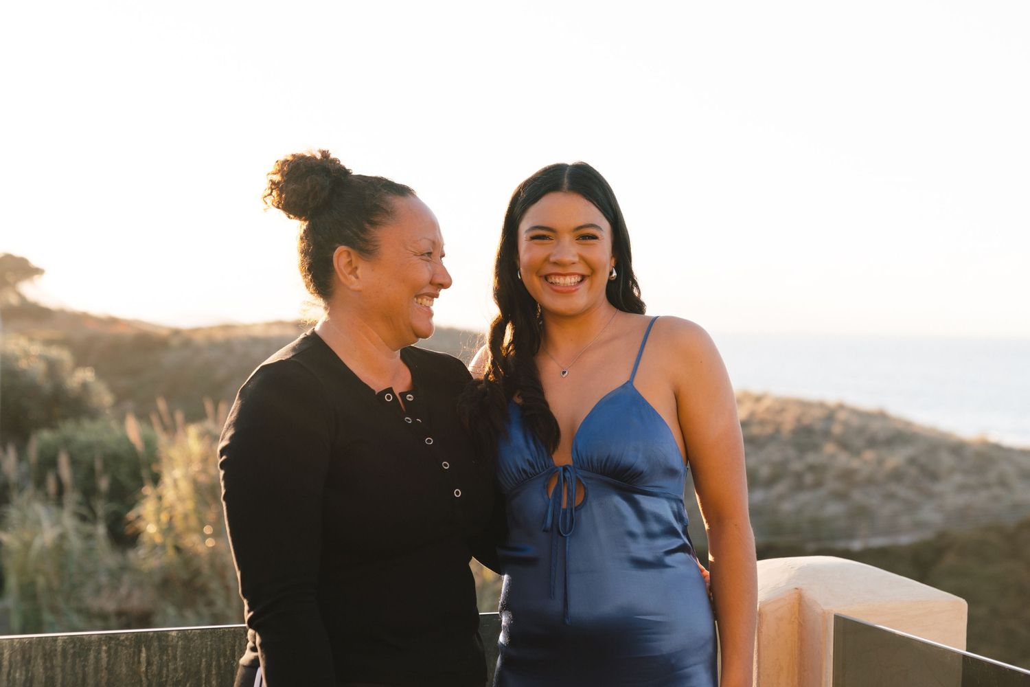 Two people share a candid laughing moment on an outdoor deck during golden hour.