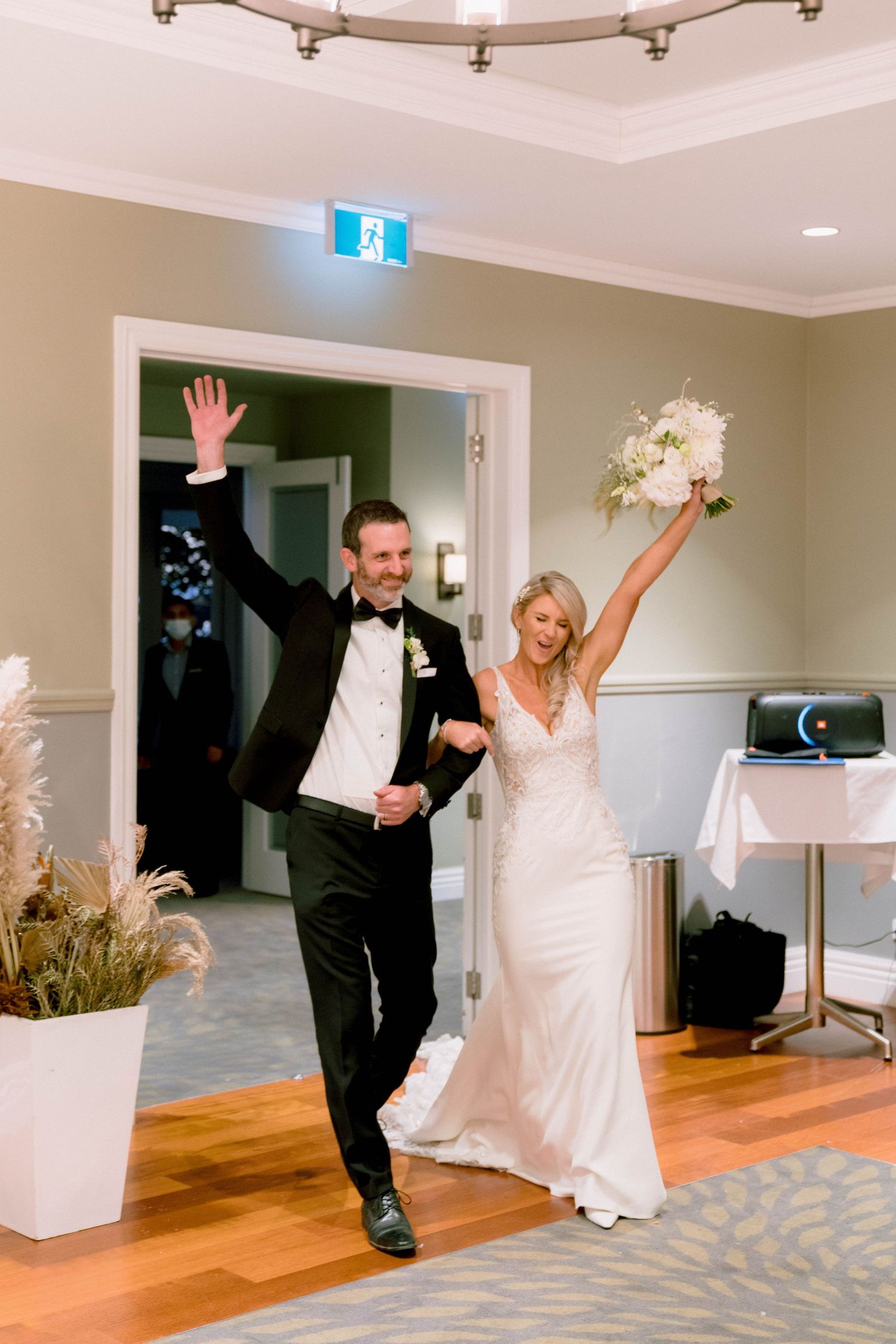 Couple in formal attire dances and spins playfully across a reception hall with hardwood floors and patterned carpet.