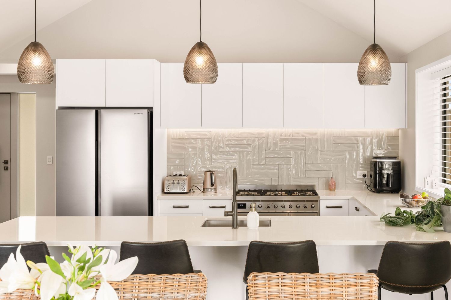 Contemporary white kitchen with pendant lighting, stone countertops and sleek cabinetry.