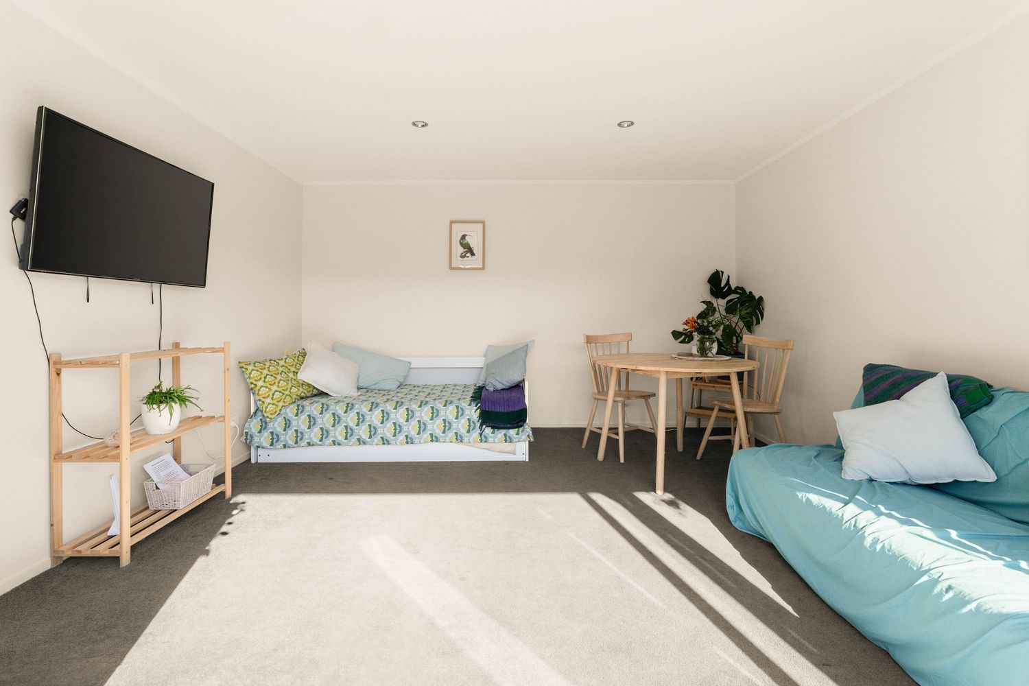 Minimalist room with wall-mounted TV, teal futon, and small dining set.