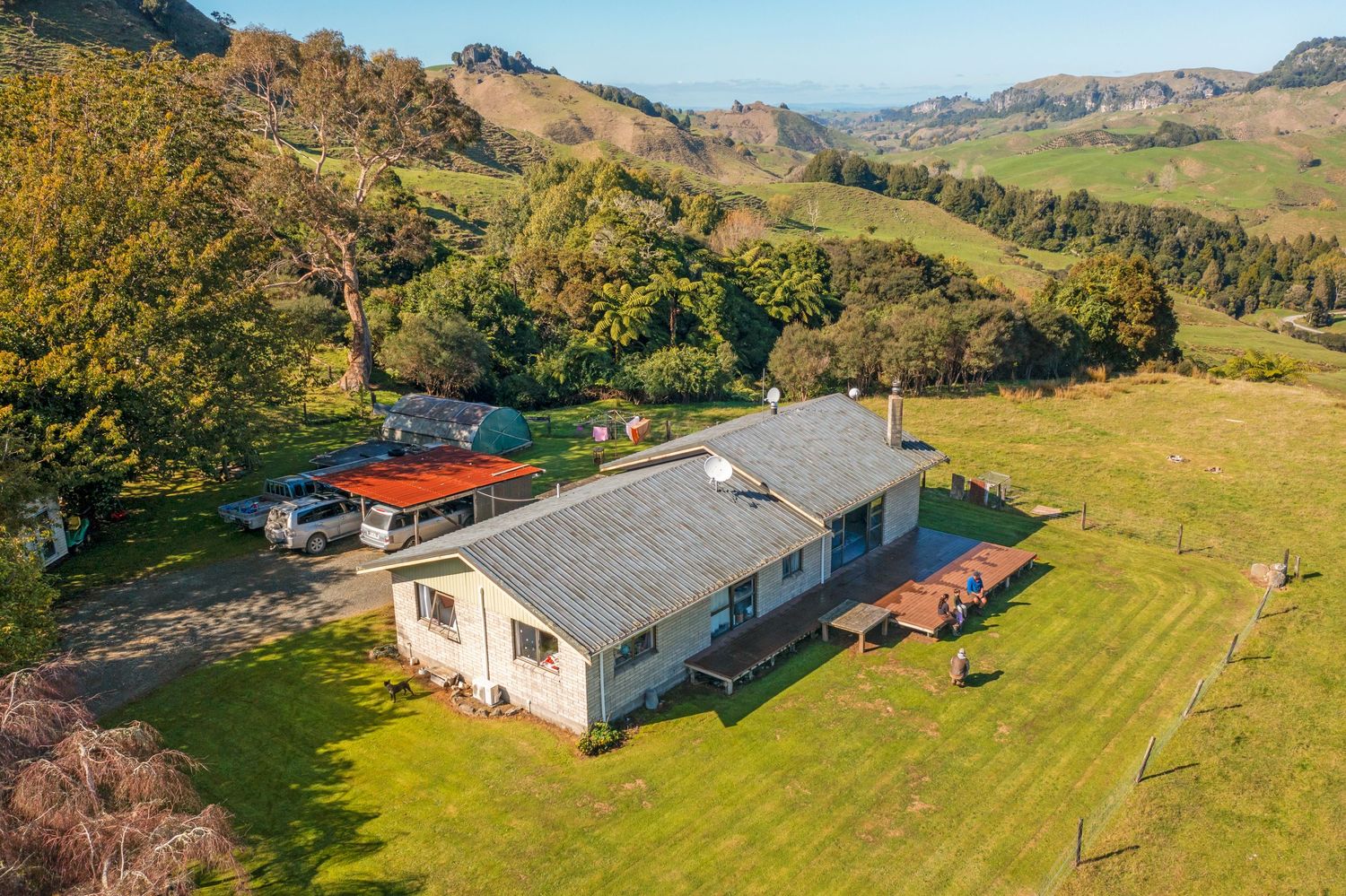 Aerial view of a ranch house nestled in rolling green hills with trees and mountains in the background.