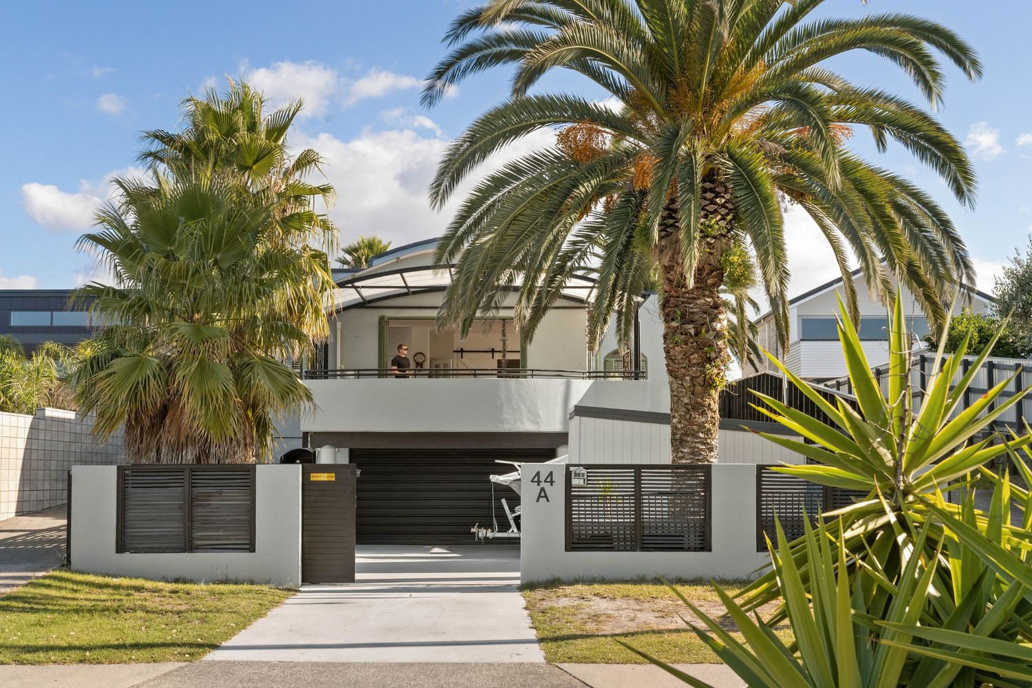 Modern two-story gray house with palm trees and contemporary architectural design featuring dark garage doors.