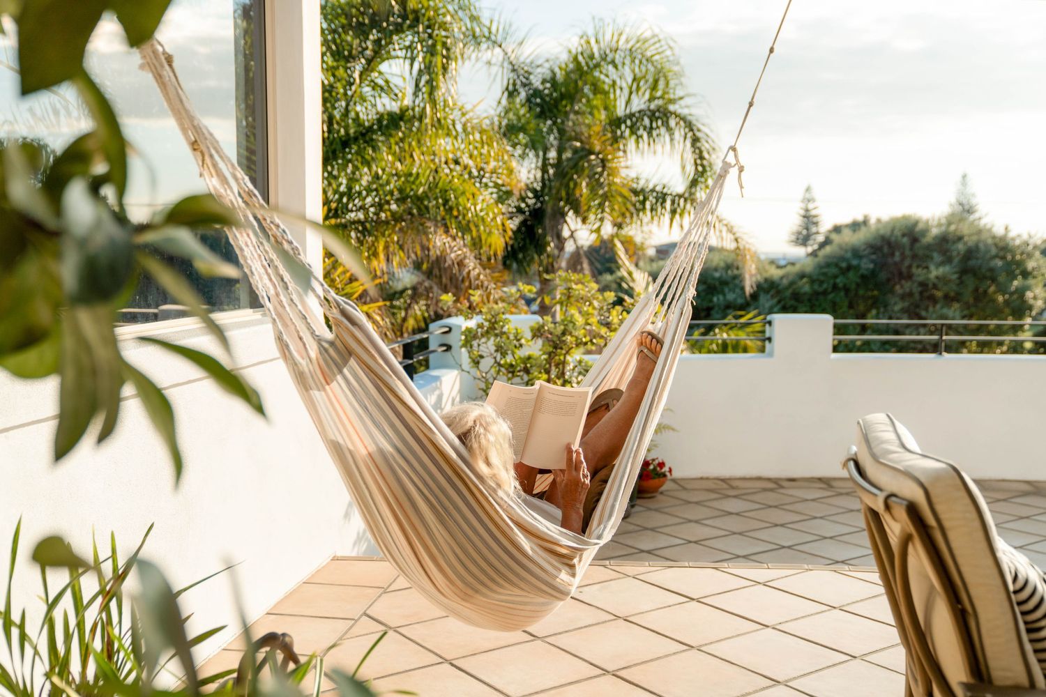 Sunny outdoor patio area featuring cozy seating arrangements surrounded by tropical palm trees and lush greenery.