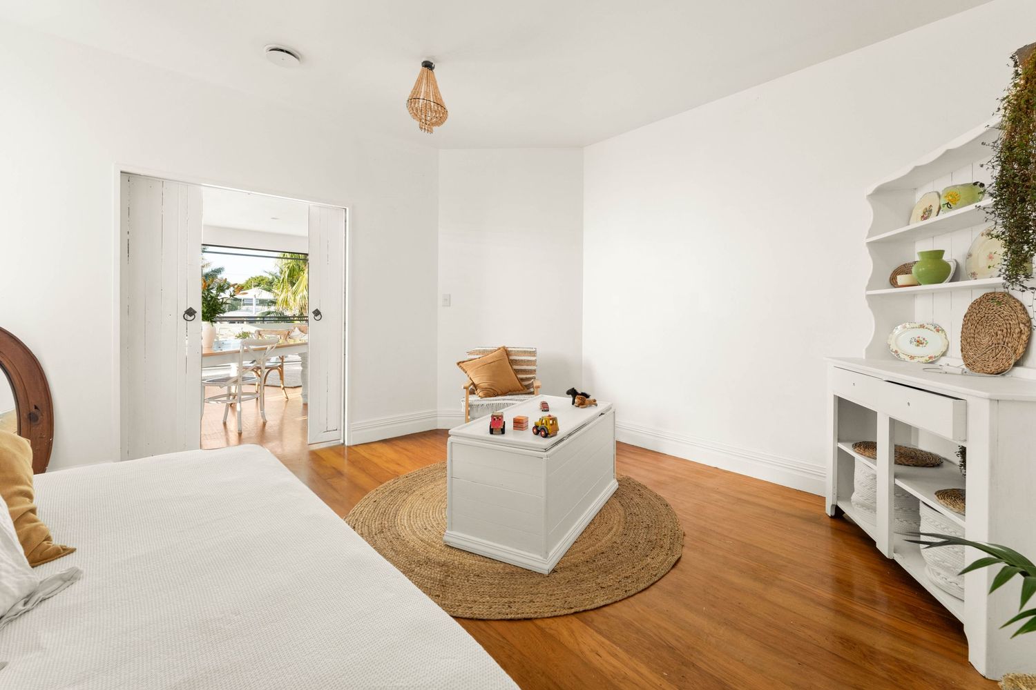Minimalist bedroom with white walls, wooden floors, and round jute rug featuring natural decor elements.