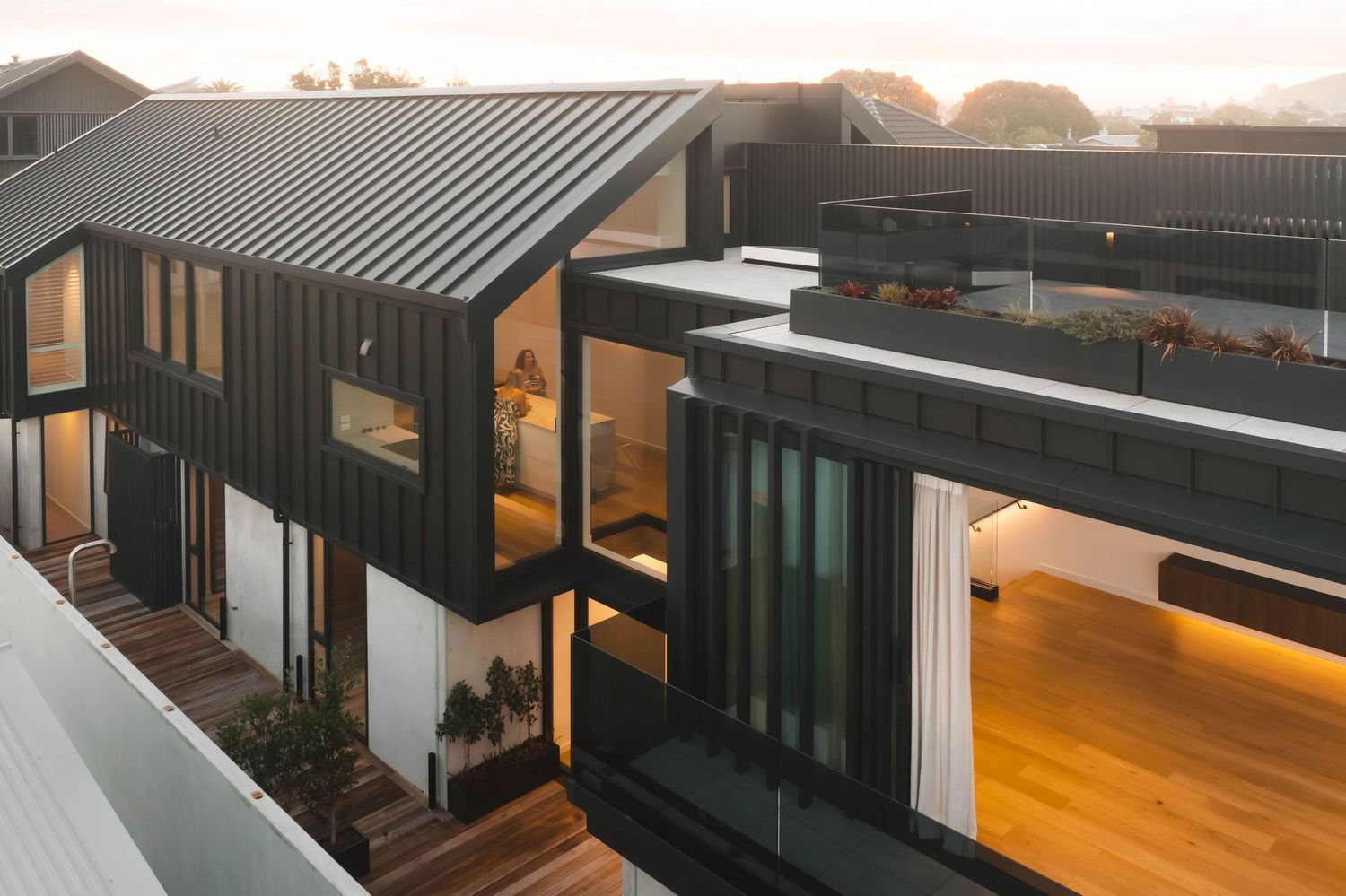 Modern house exterior with black metal cladding and warm lighting at dusk.