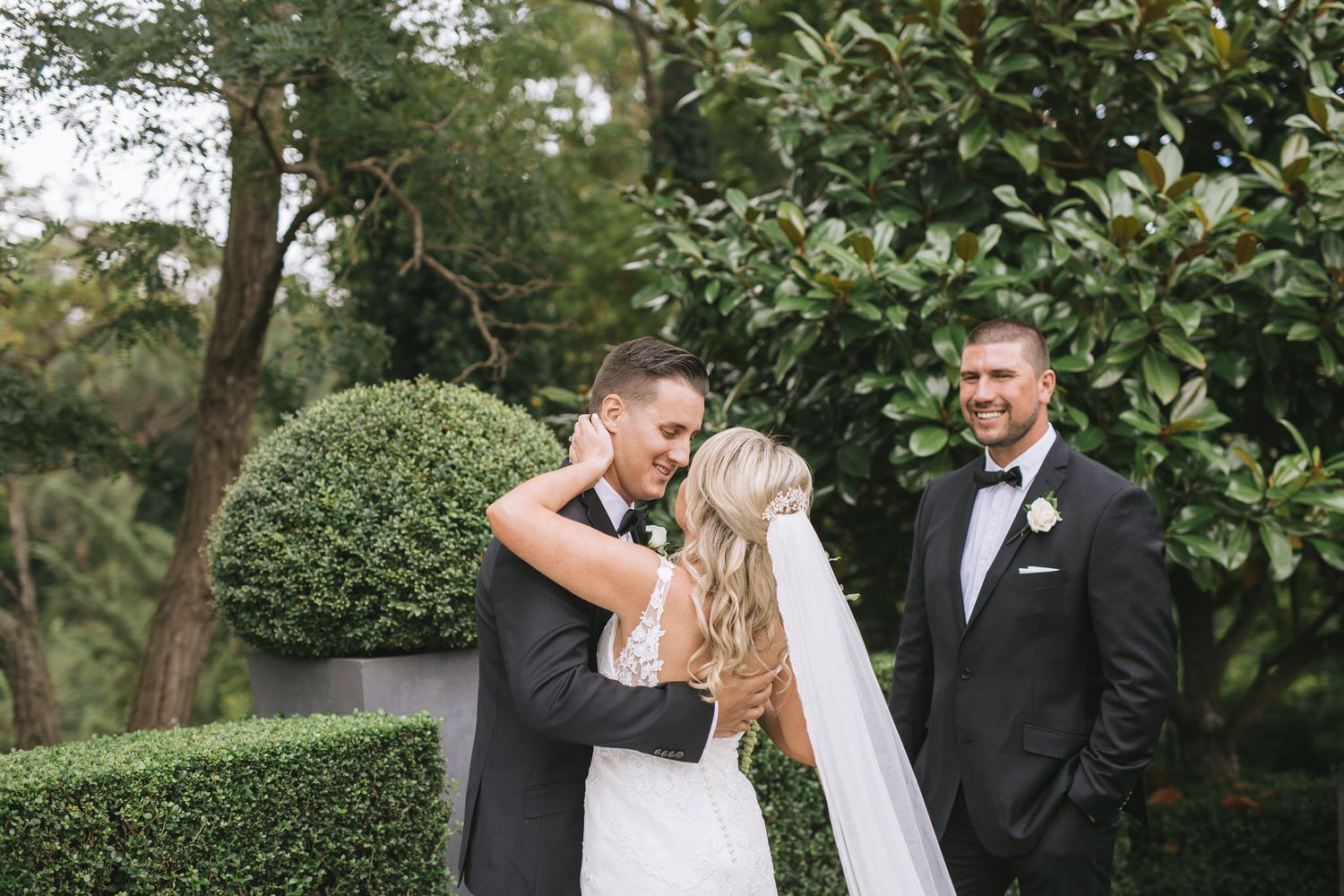 A wedding celebration in a lush garden setting with manicured boxwood hedges and greenery as backdrop.