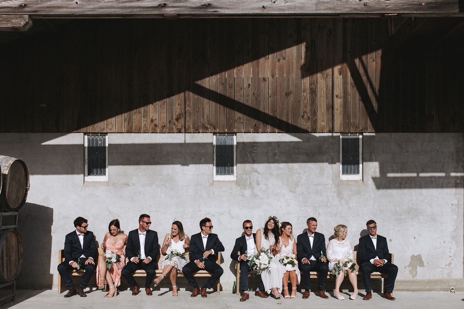 Multiple people sit in a row of chairs against a white concrete wall in a modern architectural setting.