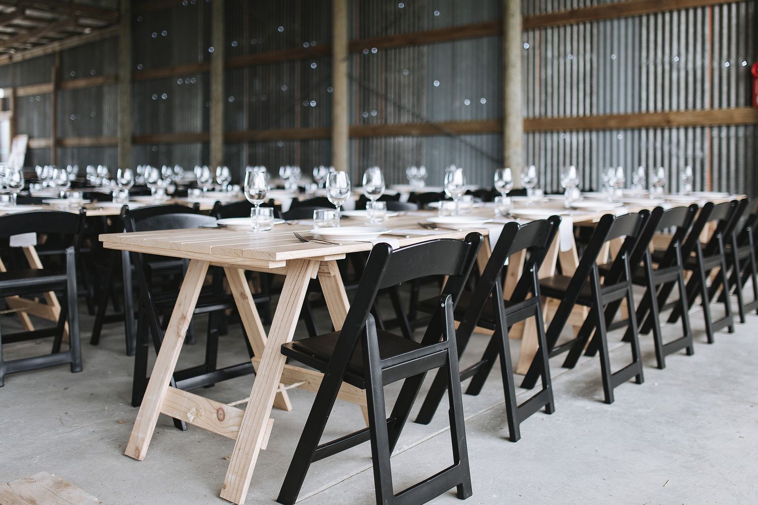 Modern cafeteria with wooden tables and black chairs arranged in long rows by metal-clad walls.