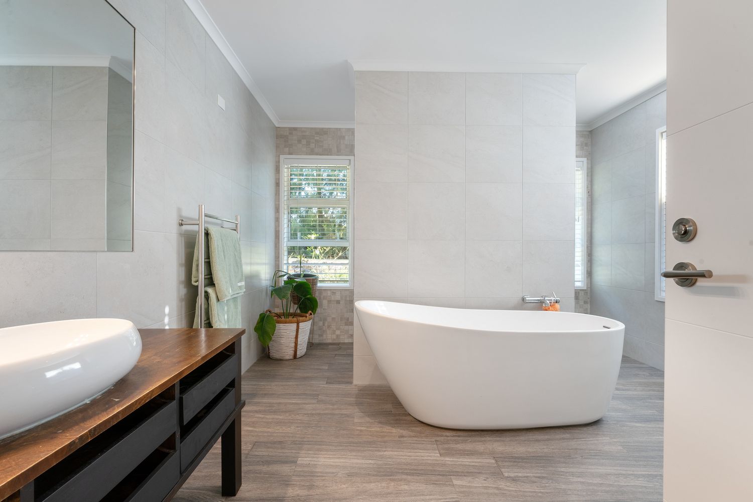 Spacious bathroom featuring freestanding tub, wooden vanity, and gray wood-look flooring.