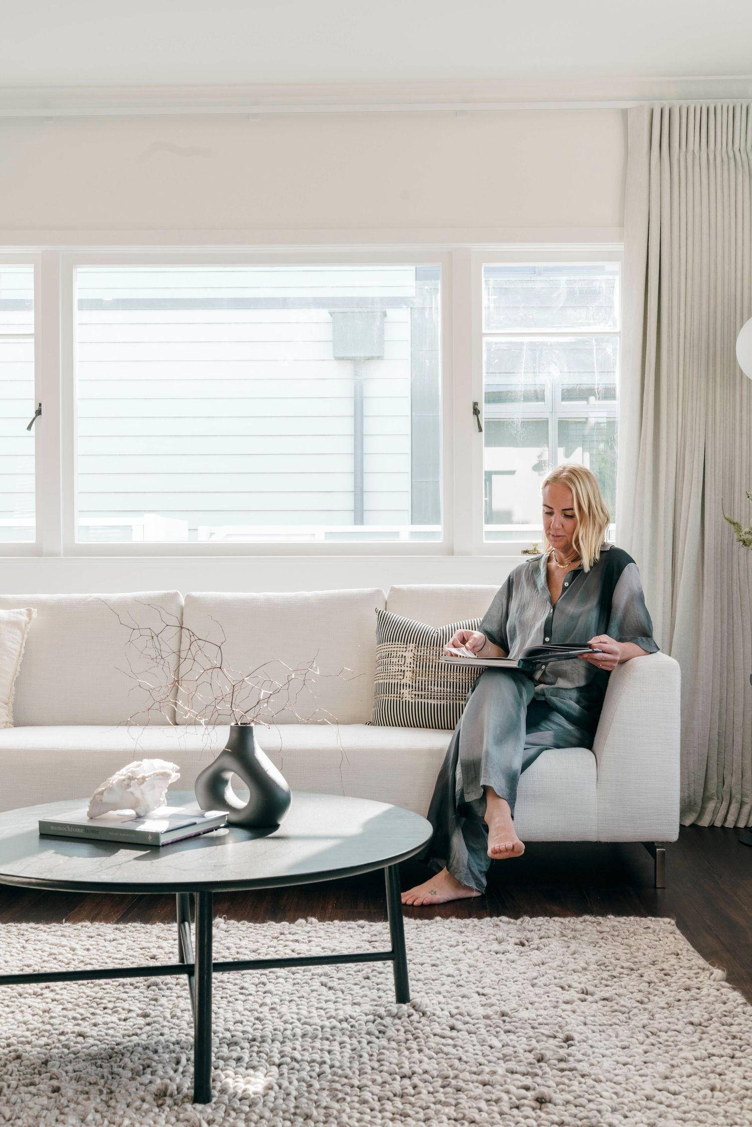 Bright modern living room with large windows, white sofa, and round coffee table on textured area rug.
