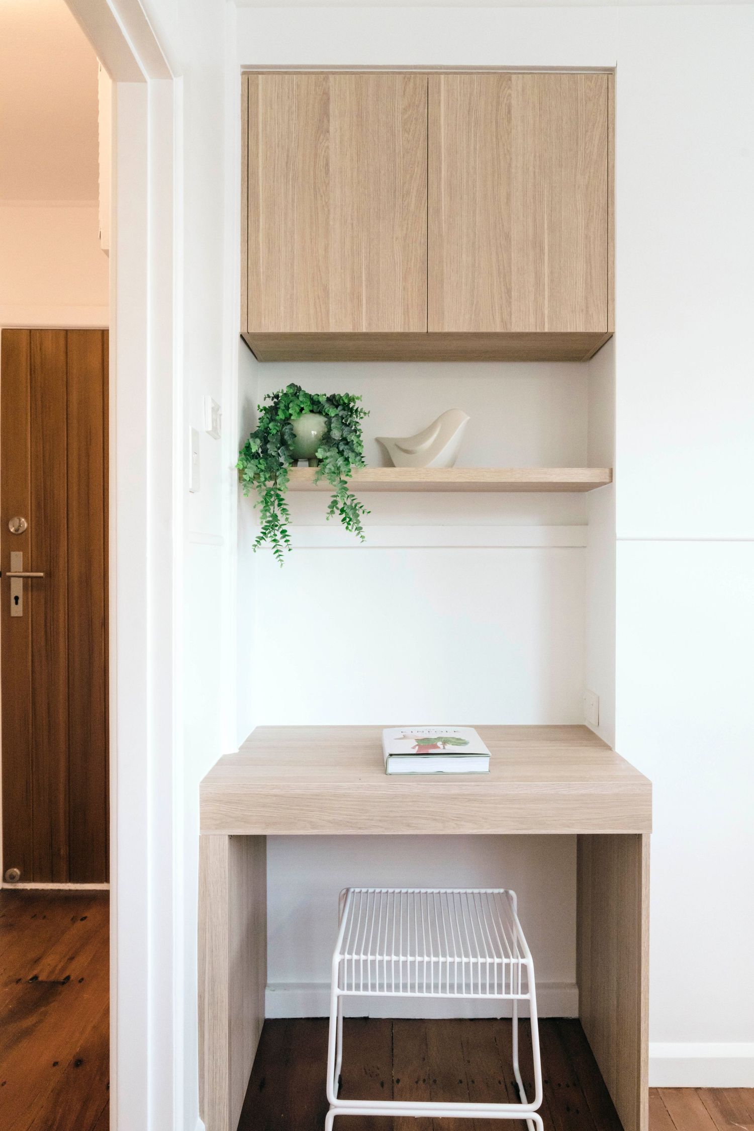 Built-in desk area with light wood cabinetry and wire mesh organizer.