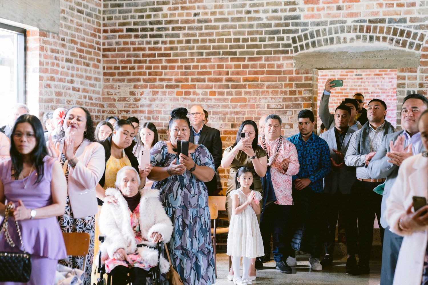 Wedding guests watch emotionally during ceremony in rustic brick venue.