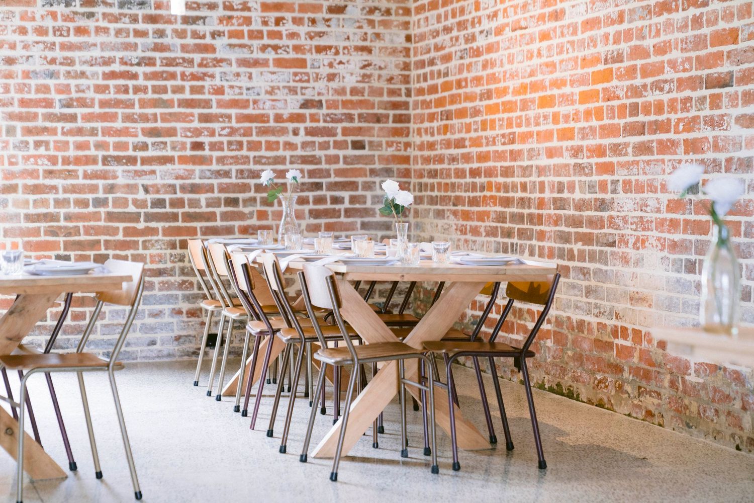 Empty reception hall with wooden tables and chairs against exposed brick walls.