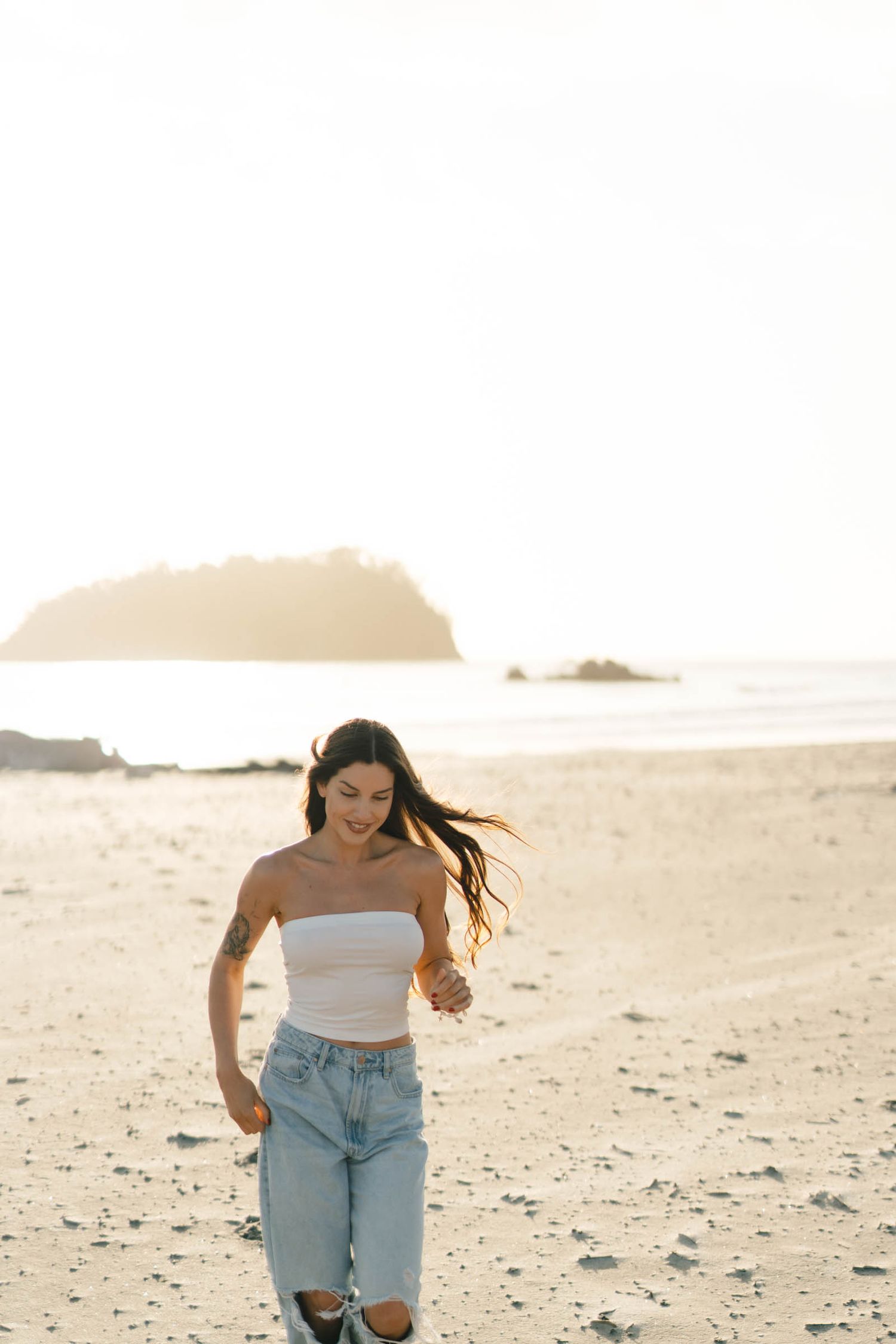 A person in casual attire runs joyfully across a sandy beach during golden hour.