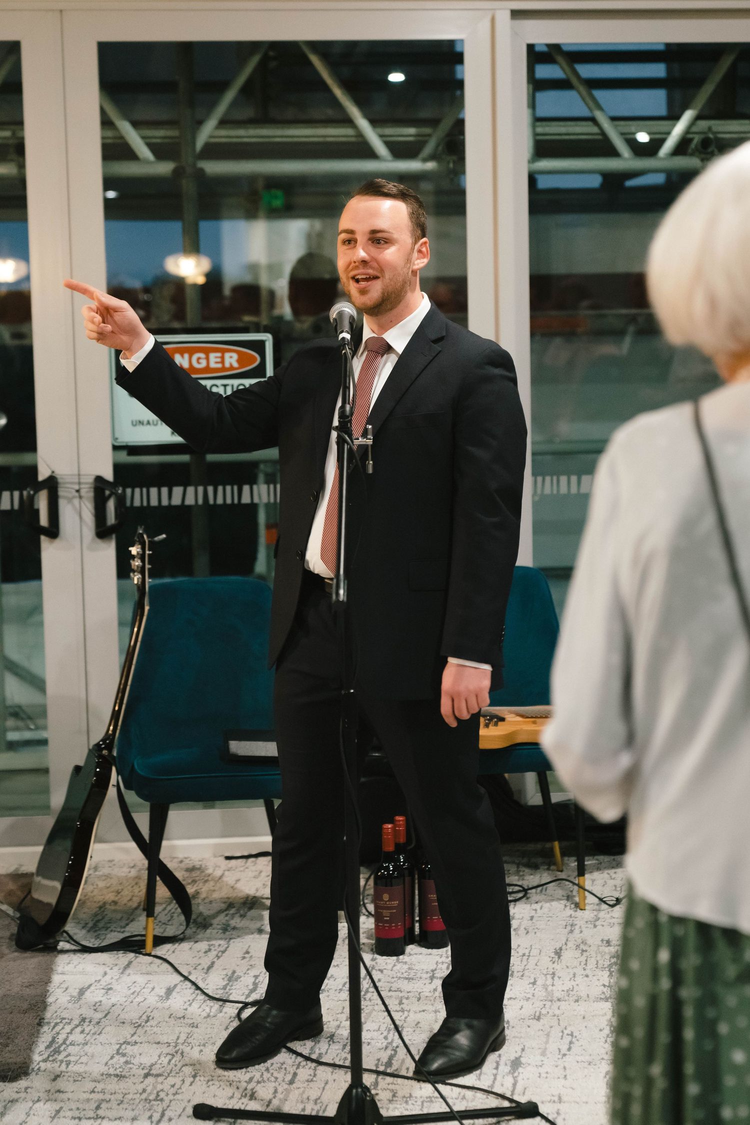 A performer in a suit gestures while standing near a microphone at an event.
