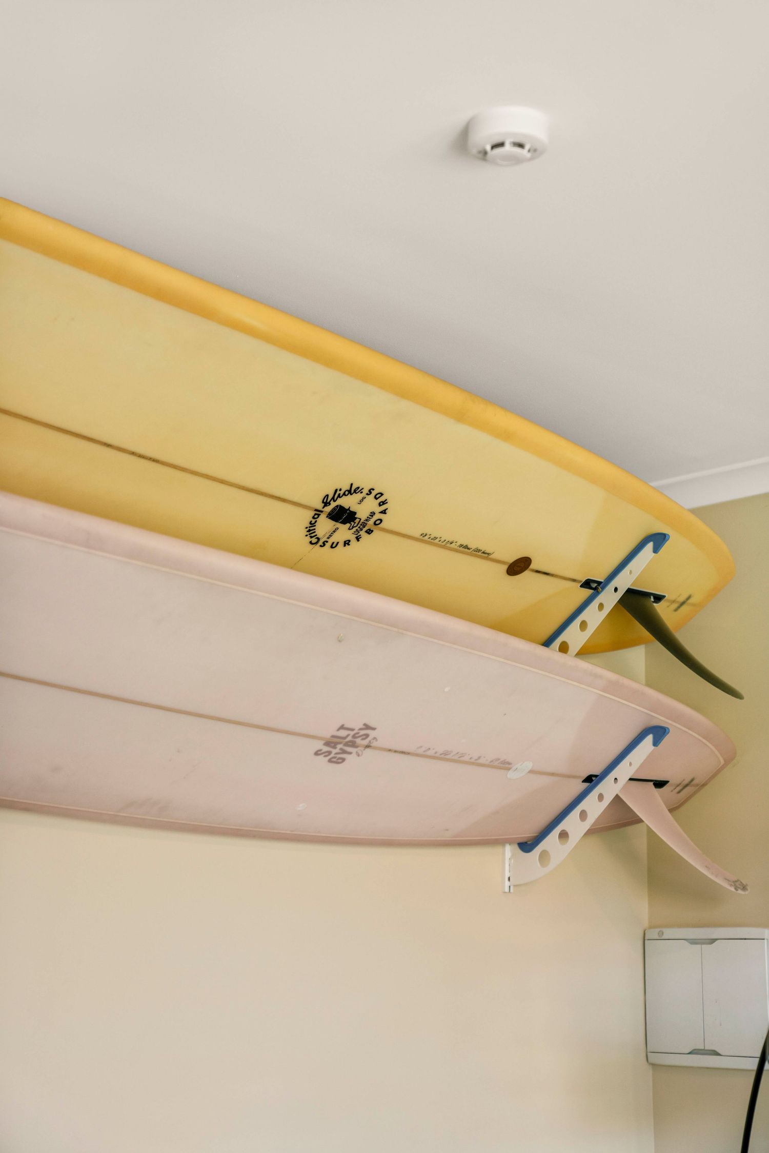 Yellow surfboard mounted on white wall with storage hooks and mounting system.