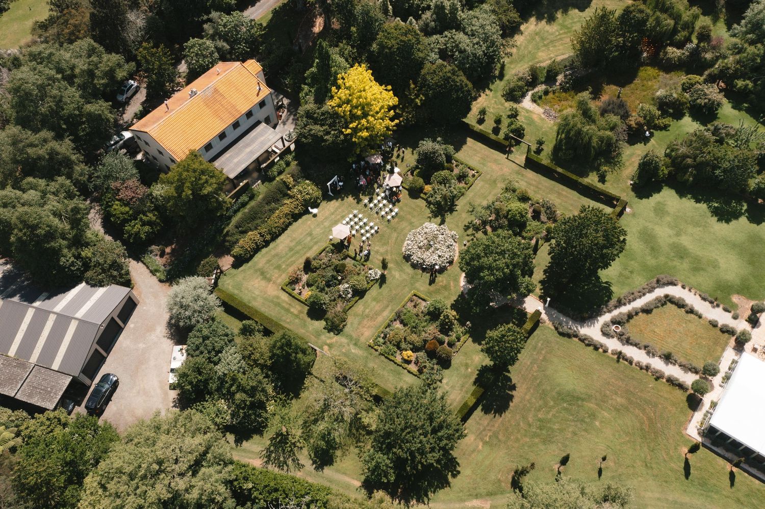 Aerial view of a wedding ceremony setup in a lush garden with white chairs and decorations.