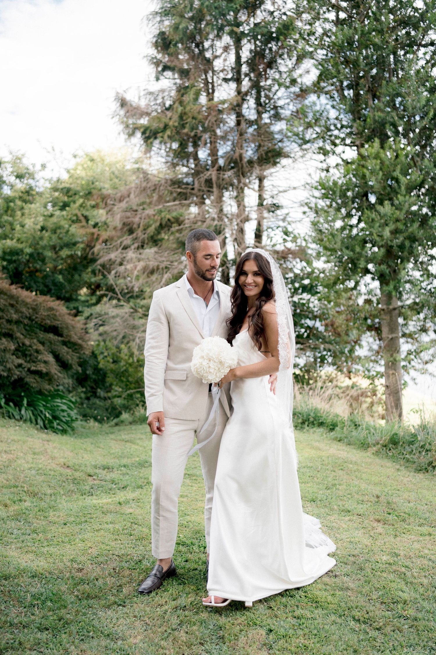 A couple in matching white outfits dancing on a grassy hillside.