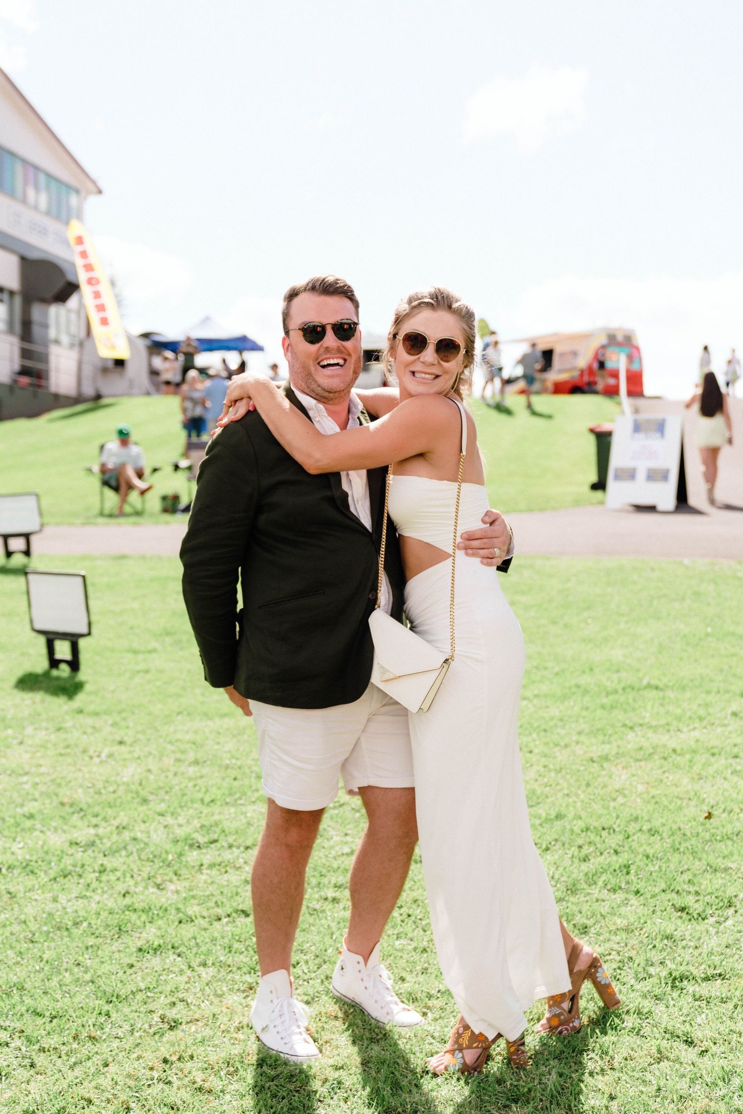Couple in coordinated black and white outfits embrace on a sunny day at an outdoor venue.