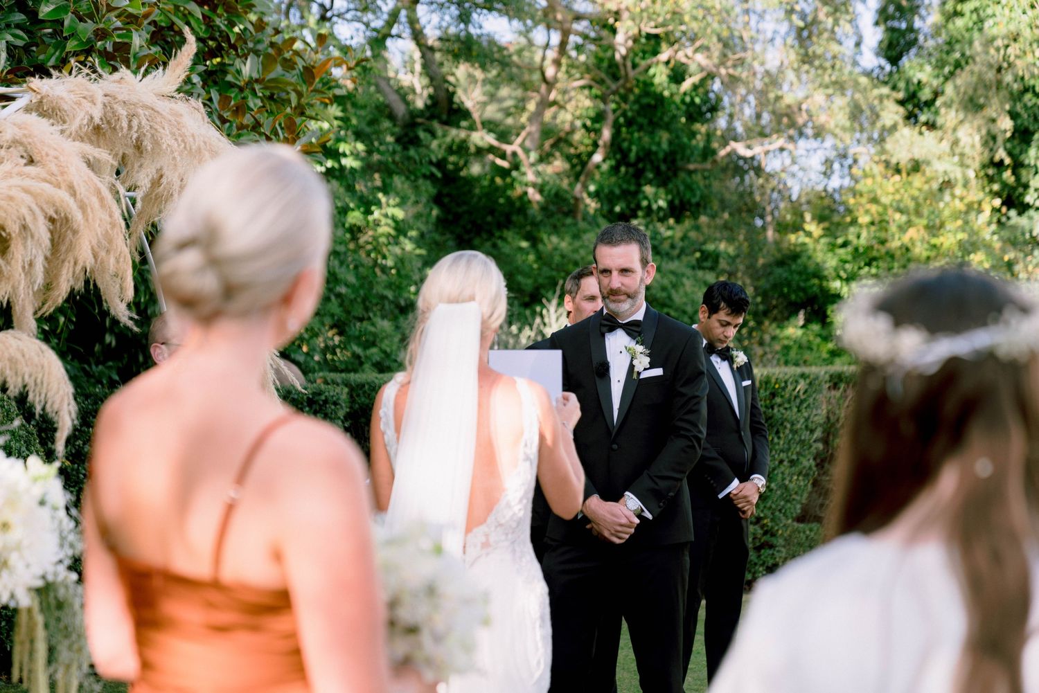 Outdoor wedding ceremony under trees with guests watching the couple exchange vows.