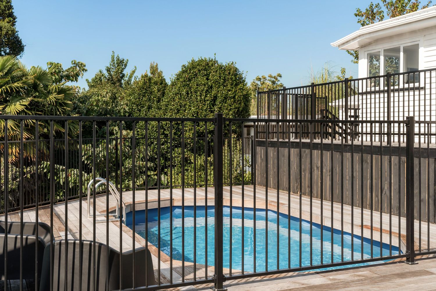 Panoramic view of backyard swimming pool with black safety fence and wooden deck.