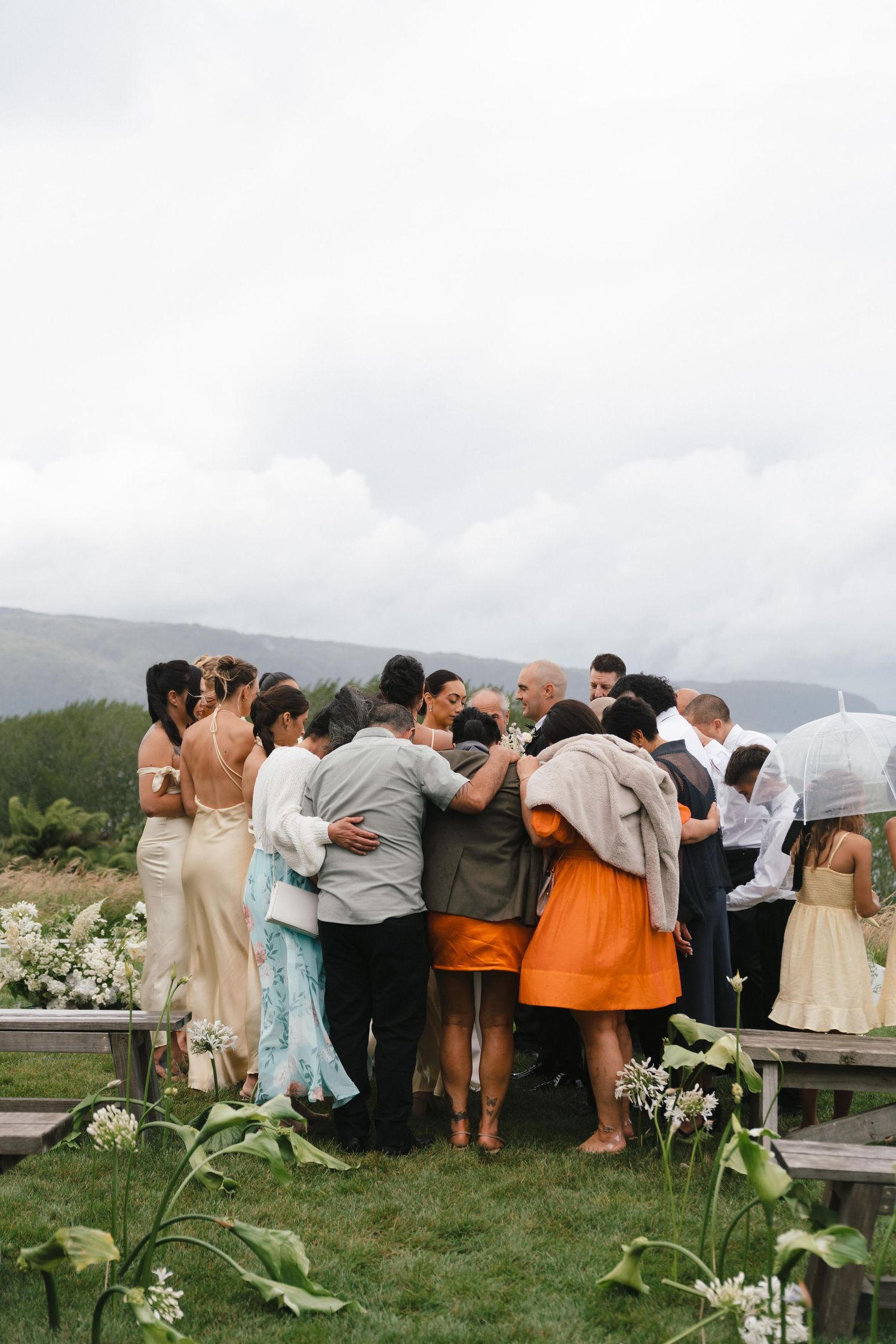 Wedding guests huddle together for a group hug on a scenic mountain overlook.