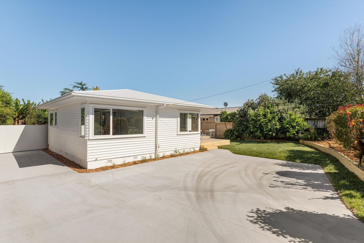 White ranch style house with curved driveway and landscaped yard on a sunny day.